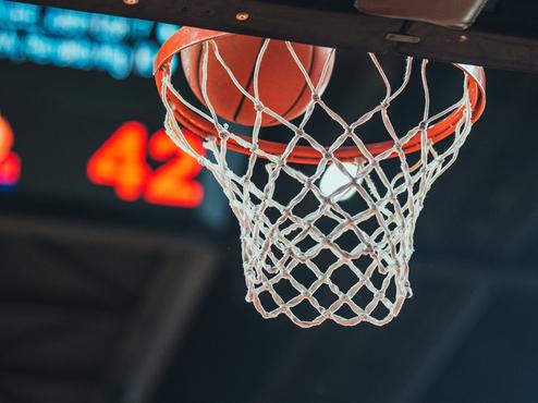 Basketballkorb mit Ball, der im Netz steckt, im Vordergrund; im Hintergrund ist die Punktzahl 42 zu sehen.