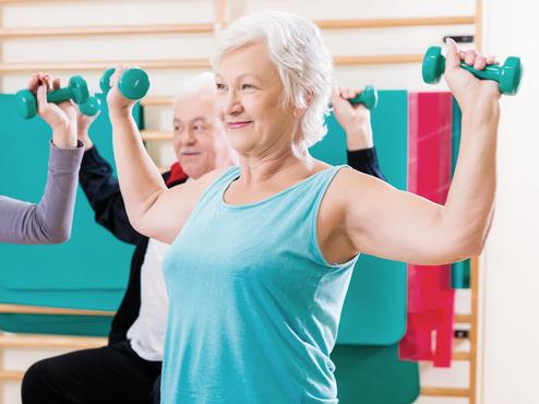 Drei Personen mit Hanteln sitzen auf großen Gymnastikbällen und trainieren in einem Fitnessraum.