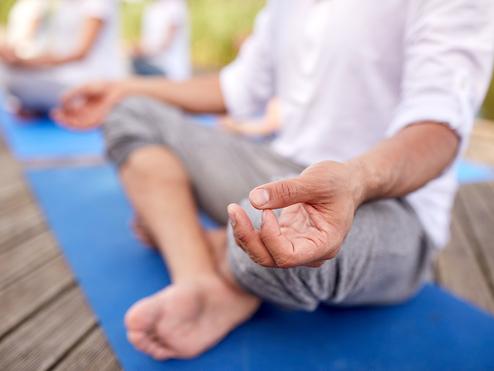 Nahaufnahme einer Hand, die im Meditationszustand auf einer blauen Yogamatte liegt, mit Fuß im Vordergrund.